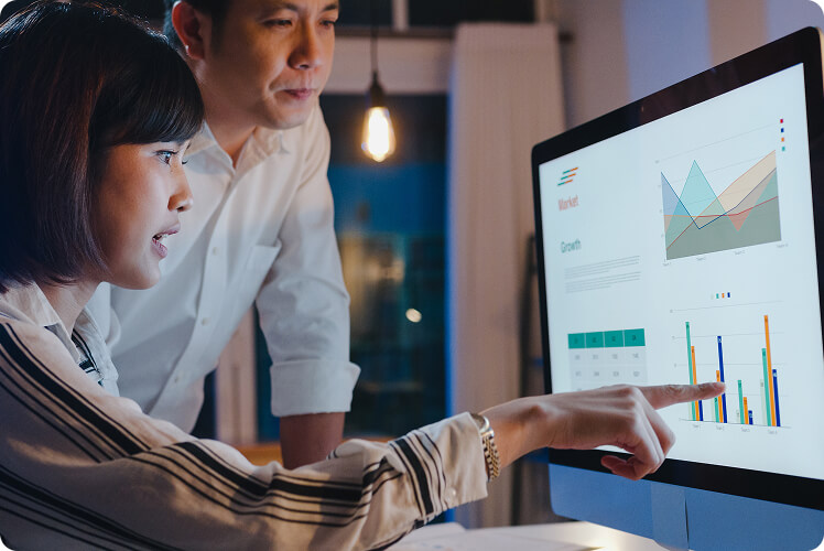 Two professionals analyzing business data and charts on a desktop dashboard