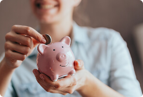 Person placing a coin into a pink piggy bank symbolizing savings and financial planning