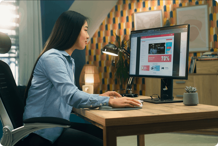 A person sits at a desk, using a computer with a colorful background, focused on an online shopping website displaying a sale.